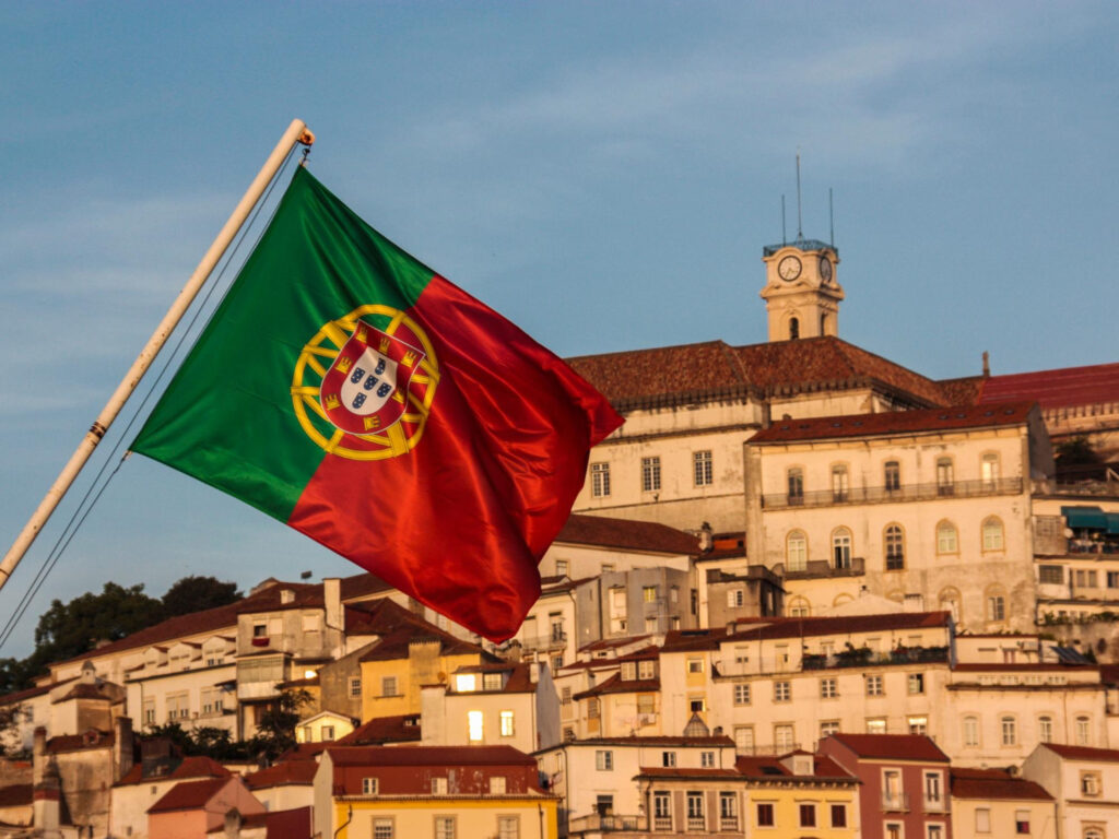 Flag of Portugal waving in front of historic buildings and traditional Portuguese architecture.